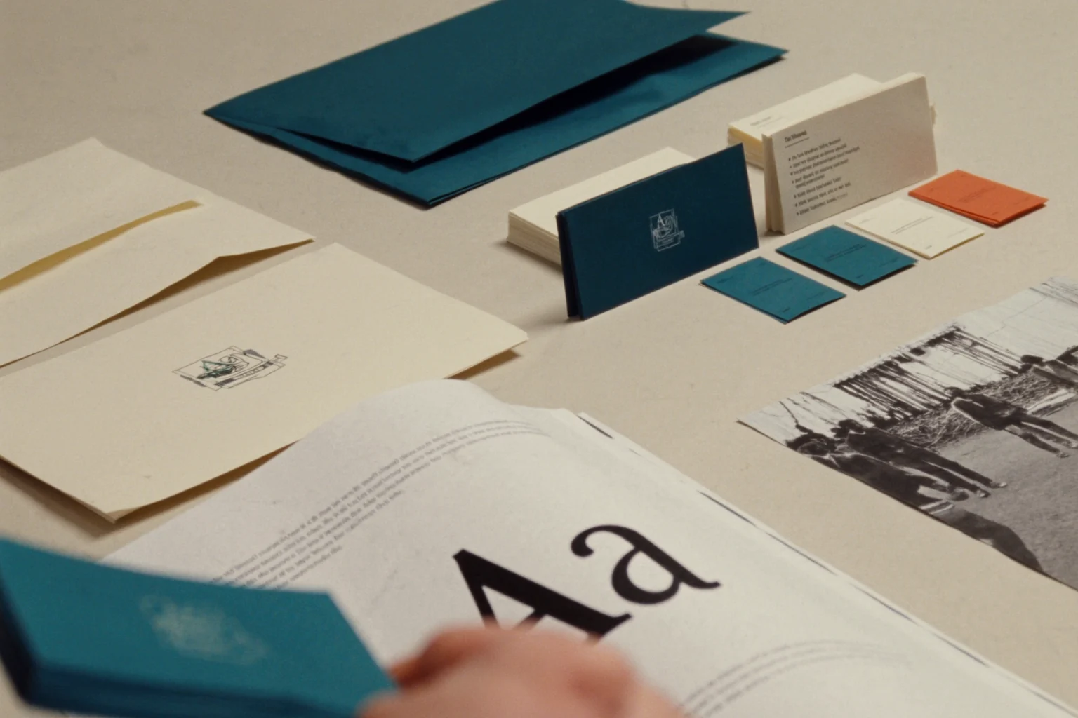 Stationery laid out on a table: teal envelopes and folders, business cards, color swatches and a printed page with a large Aa.